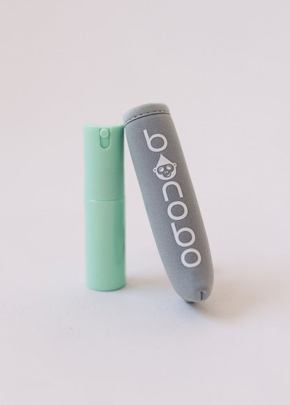 Hands demonstrating spray usage onto a wipe during a diaper change, illustrating one-handed operation and spill-resistant nozzle design for parents.