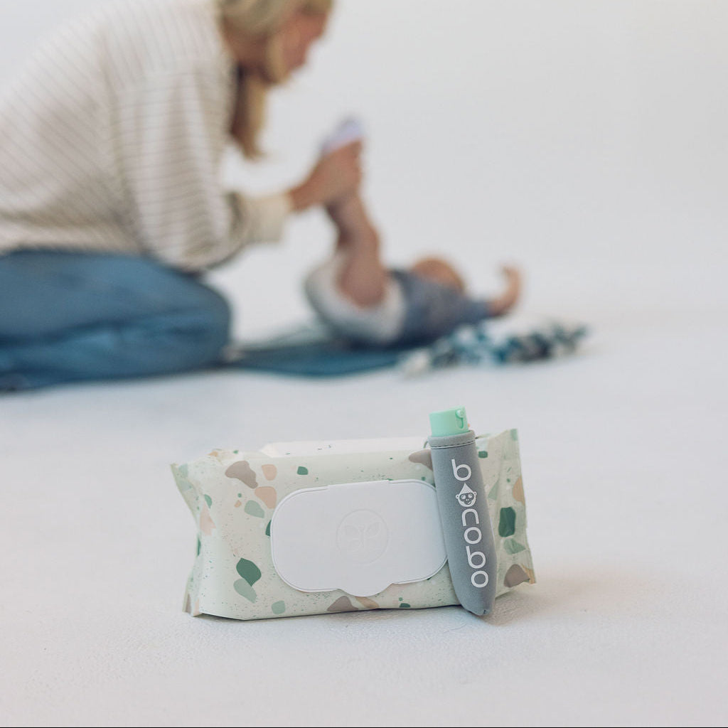 Baby wipes with a visible brand logo on a white surface, with a blurred background of a woman and child.
