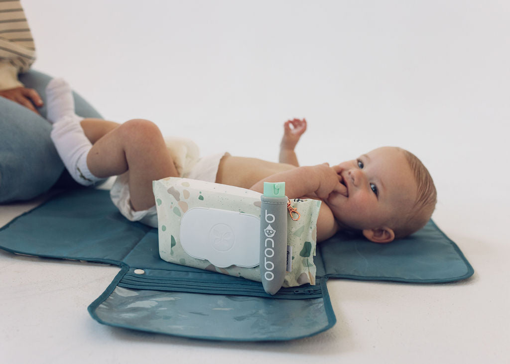 Top-down scale view of the pouch with elastic band wrapped around a wipe package and the 20ml bottle partially inserted showing fit and size.