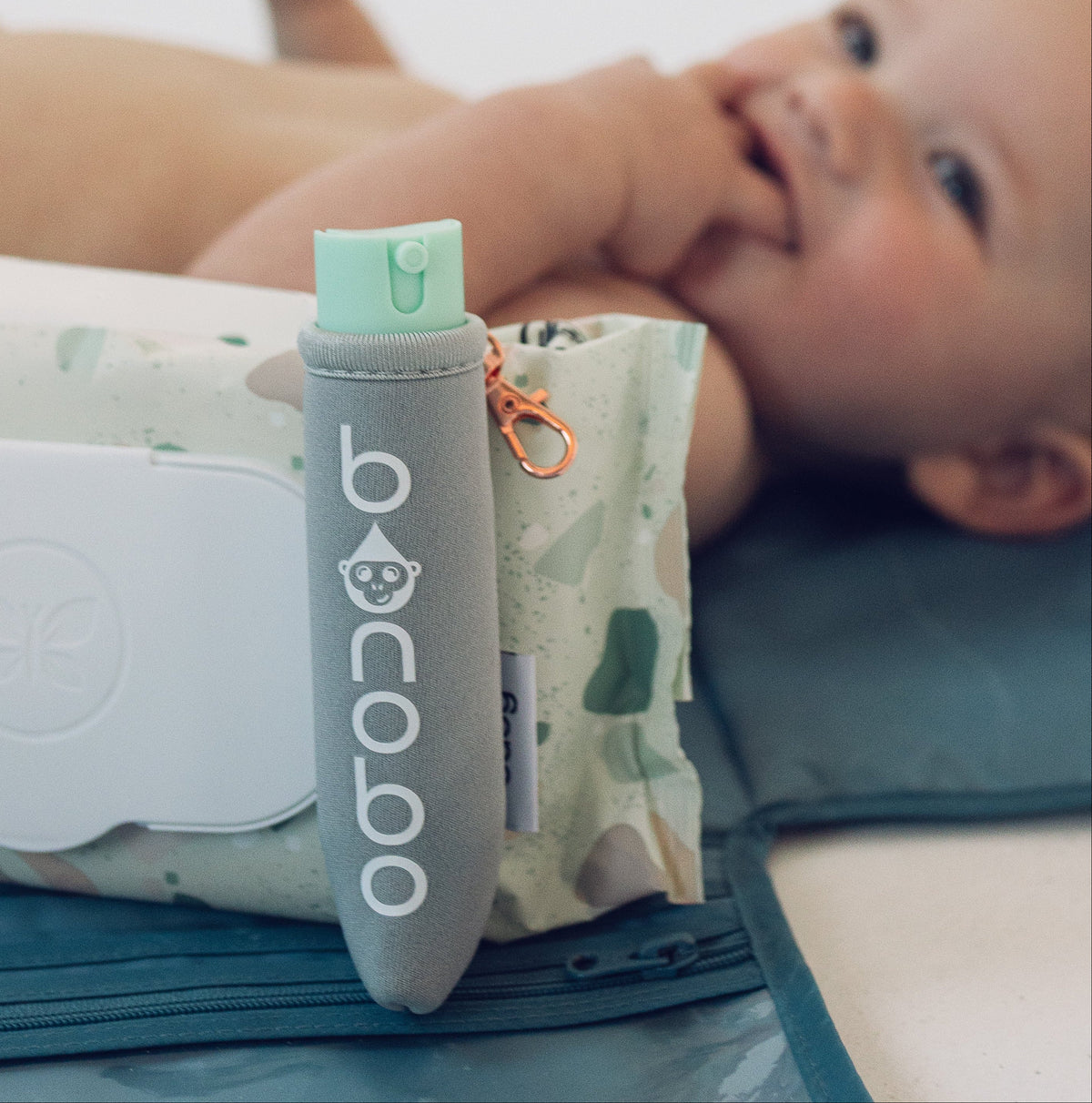 Baby on a changing pad next to a wipes pack with the Bonobo baby bidet