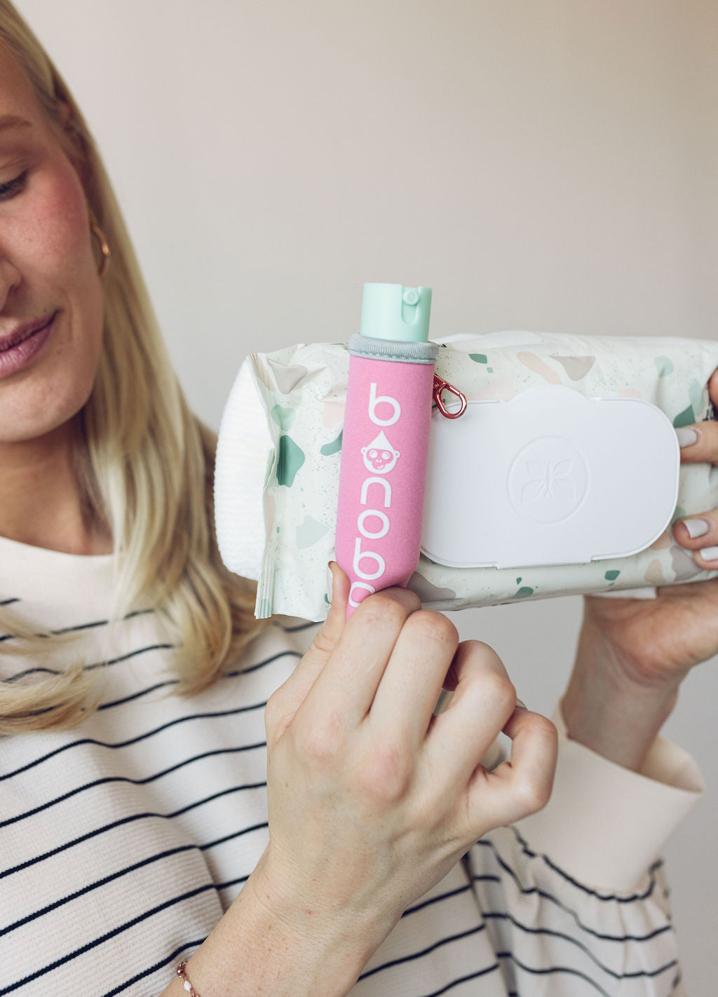 Spritzer pouch attached to a standard wipes pack with elastic band stretched around, demonstrating universal fit and hands-on use.