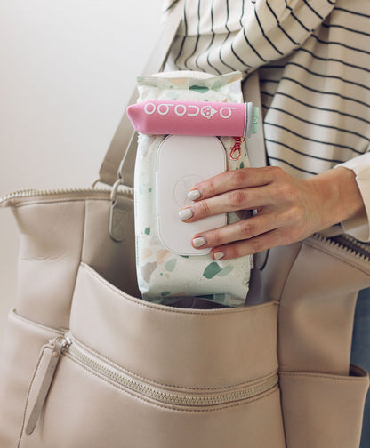 Top-down view of the neoprene wipes pouch loaded with a wipes packet and the 20ml spritzer partially inserted for one-handed use demonstration.