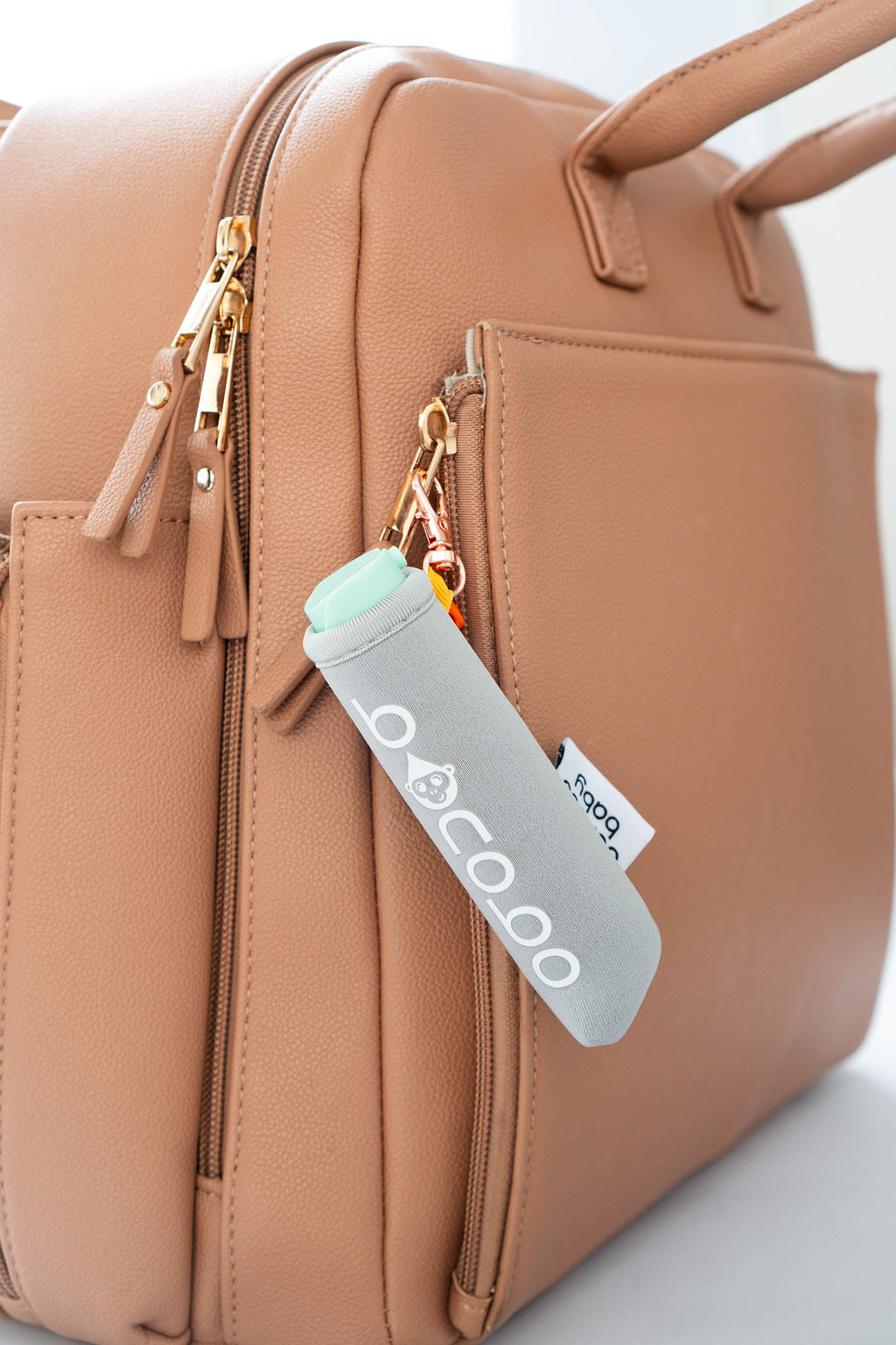 Side-angle photo of neoprene pouch and 20ml bottle showing size and soft edges and ability to clip to diaper bag 